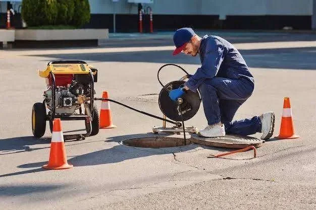 Homem de uniforme azul operando máquina desentupidora em bueiro aberto com cones de segurança