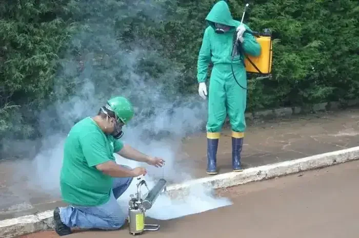 Dois homens com equipamentos de proteção individual realizam nebulização em área externa